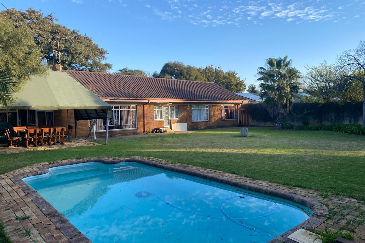 Rear view of the house featuring a swimming pool, brick-paved surround, covered patio area, and a spacious lawn.