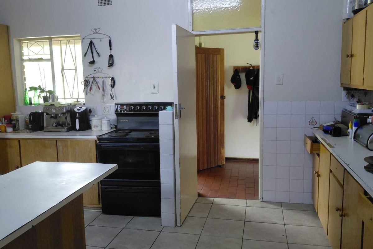 A functional kitchen featuring wooden cabinetry, tiled splashbacks, and a freestanding stove, offering a dated layout with potential for modern renovation.