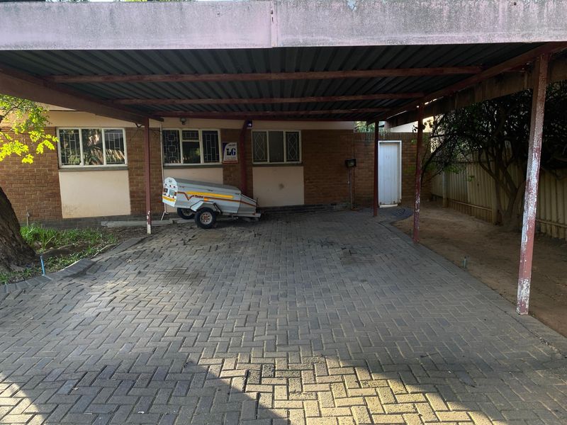 A covered carport area with paved driveway and brick exterior walling, showing signs of wear and maintenance requirements.