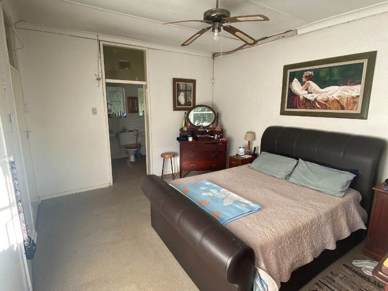 A bedroom featuring carpet flooring and a ceiling fan, with direct access to an en-suite bathroom. The room requires cosmetic updates and ceiling repairs.
