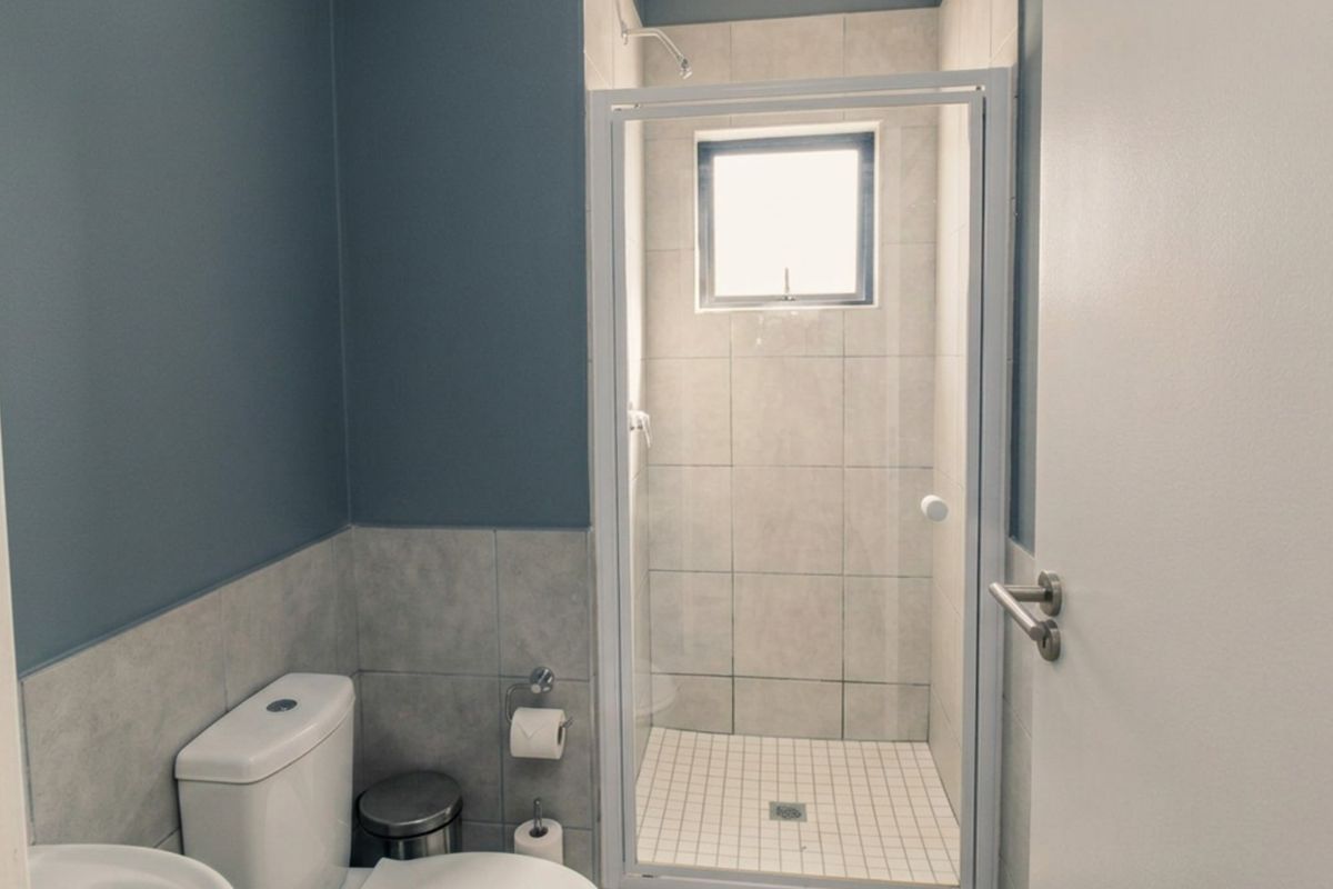 A functional bathroom featuring a tiled shower enclosure, modern toilet, and neutral wall finishes with a small window for natural light.