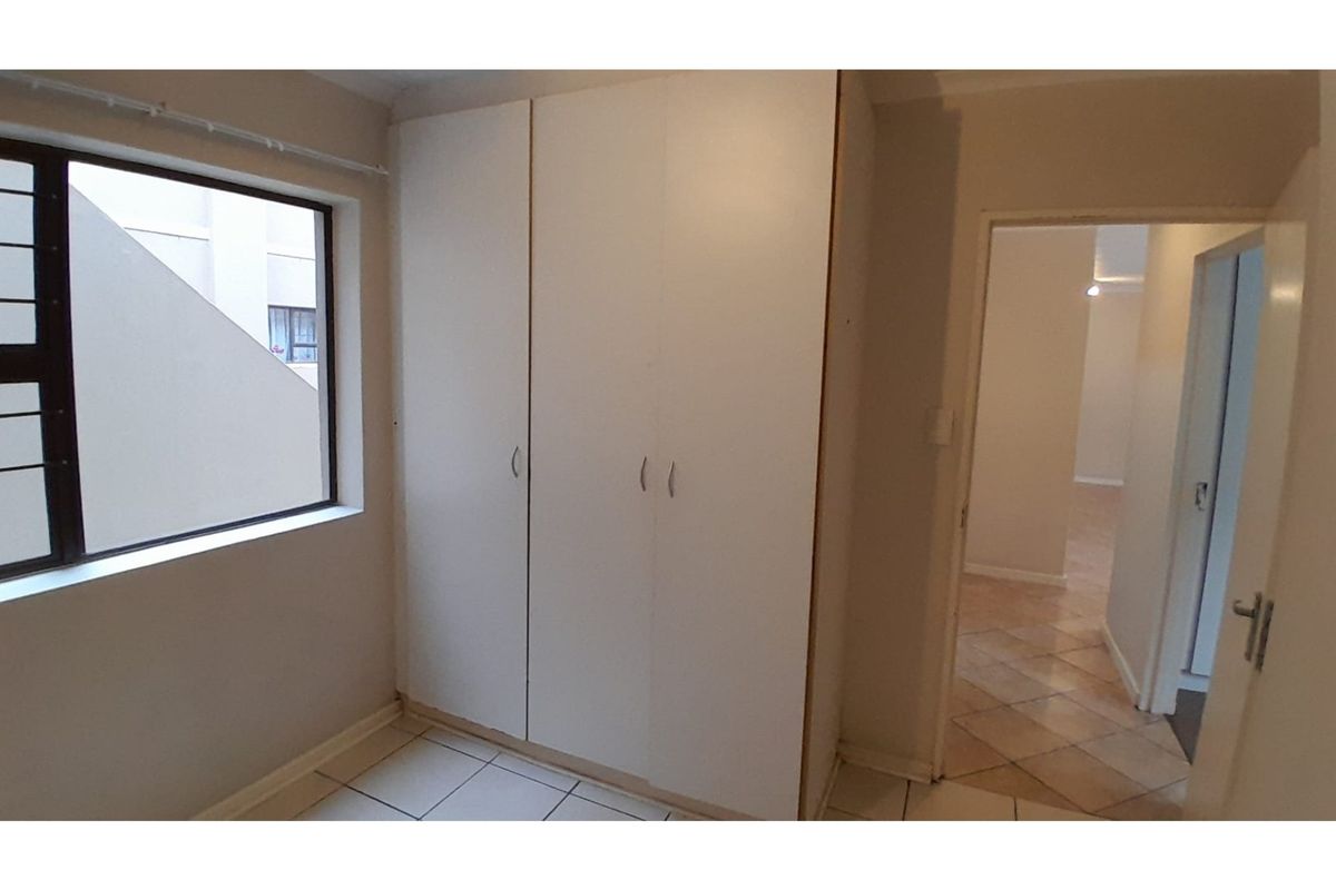 A bright, empty bedroom featuring built-in cupboards, tiled flooring, and a window with an exterior view.