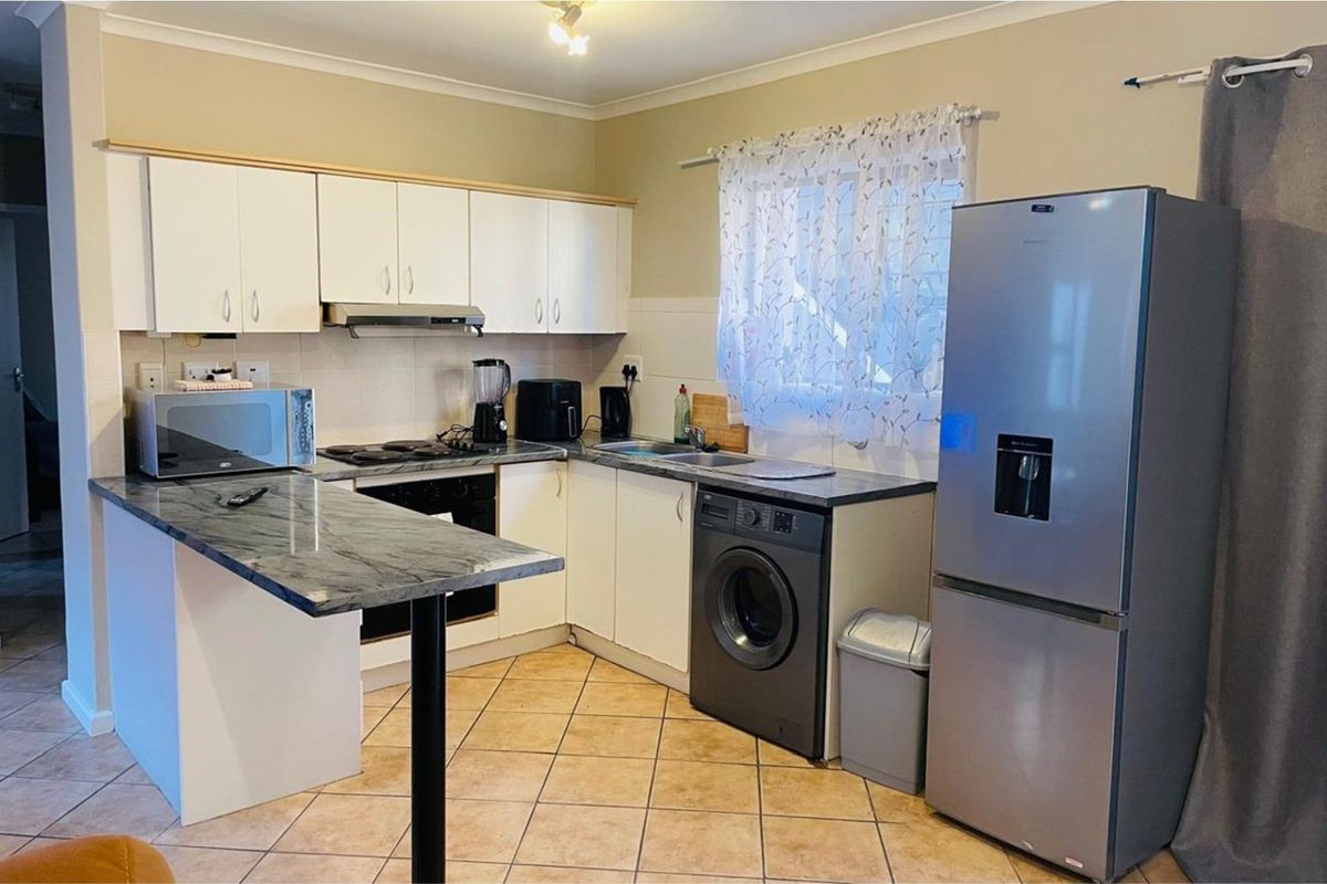 A functional kitchen featuring white cabinetry, dark stone-look countertops, an electric hob, and tiled flooring, providing a practical layout for daily meal preparation.