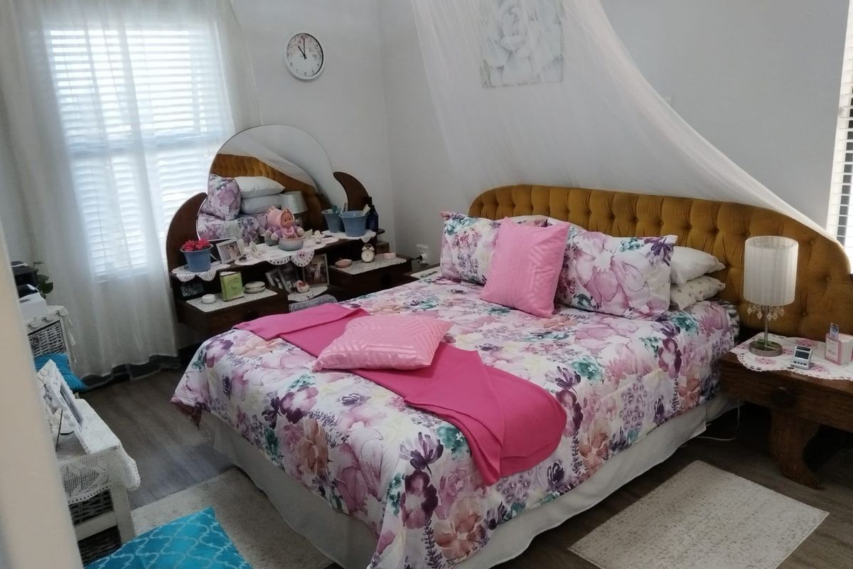A well-maintained bedroom featuring wood-look flooring, neutral wall finishes, and large windows with fitted blinds, providing a comfortable living space.