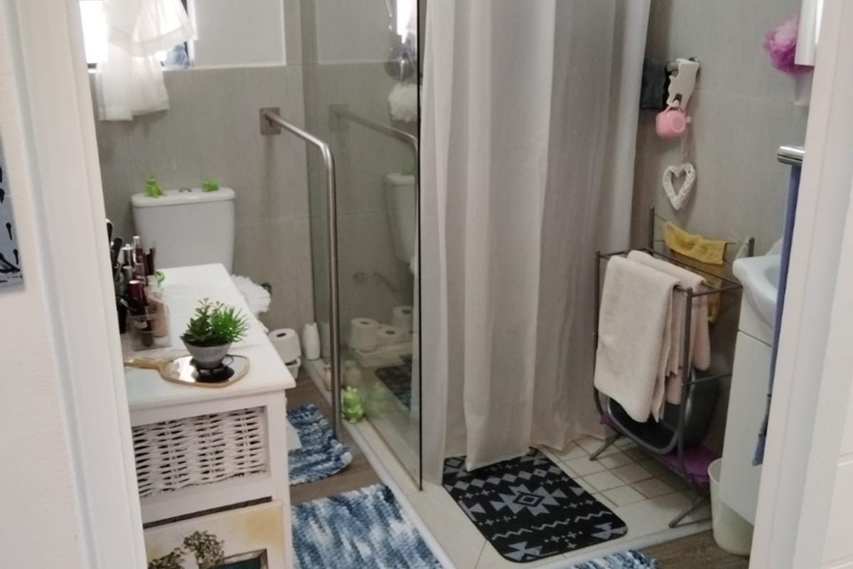 A functional bathroom featuring a glass-enclosed shower with a grab rail, a toilet, and a vanity basin with neutral wall tiling.