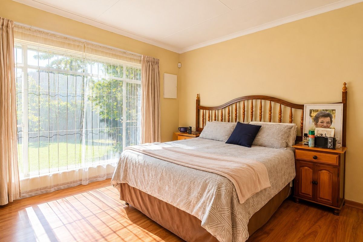 A bright bedroom featuring laminate flooring, large windows with security bars, and direct access to the garden area.