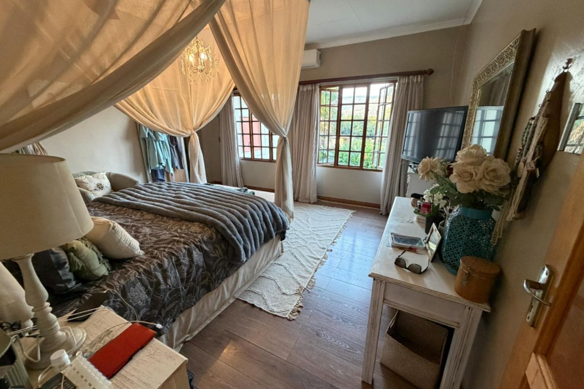 A cozy bedroom featuring wood-look flooring, large windows with natural light, and a wall-mounted air conditioning unit.