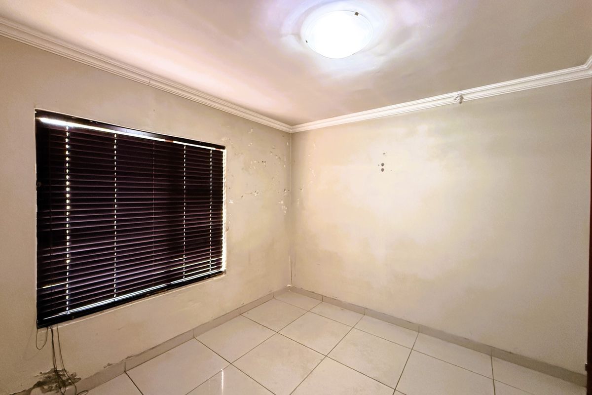 An empty bedroom featuring tiled flooring, venetian blinds, and ceiling cornice, currently requiring wall repairs and repainting to restore its condition.