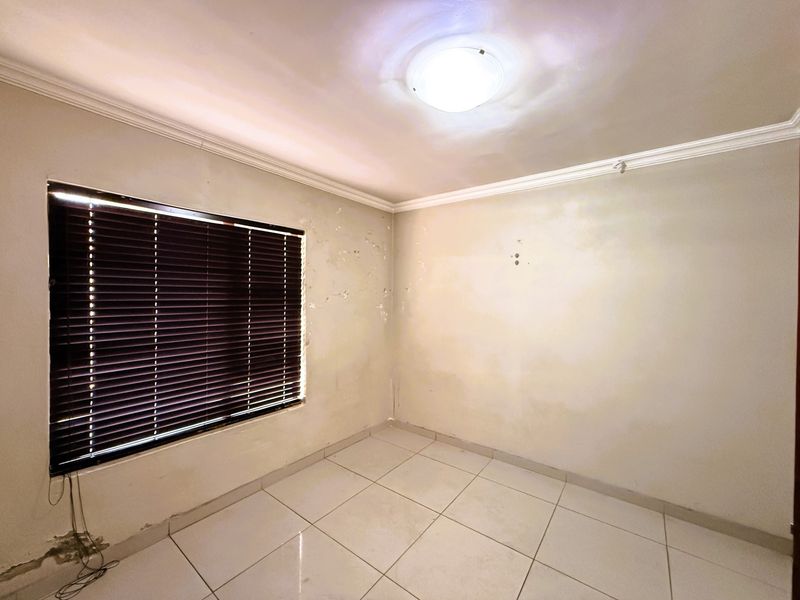 An empty bedroom featuring tiled flooring, venetian blinds, and ceiling cornice, currently requiring wall repairs and repainting to restore its condition.