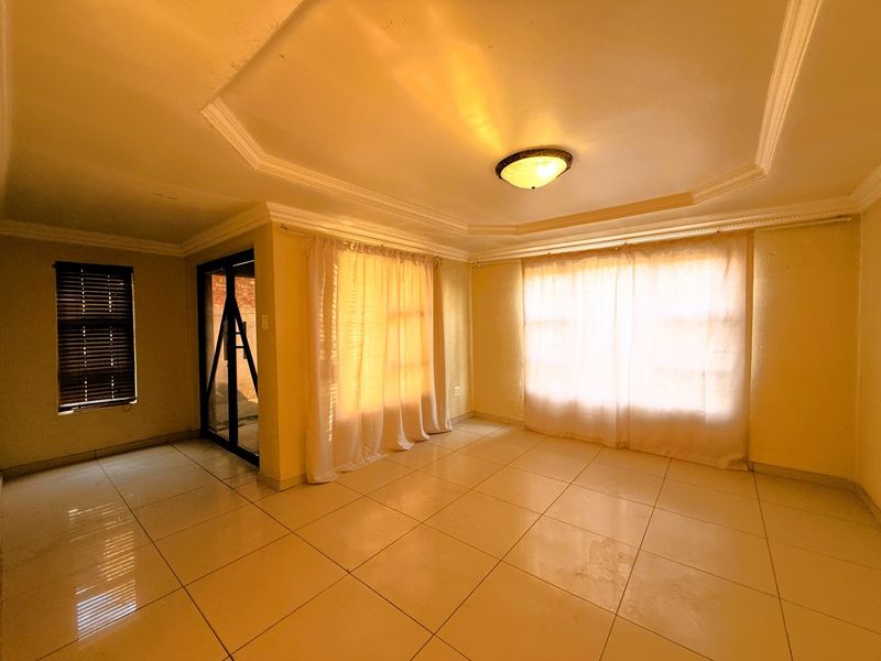 An empty living room featuring tiled flooring, a recessed ceiling with a central light fixture, and large windows with curtains.