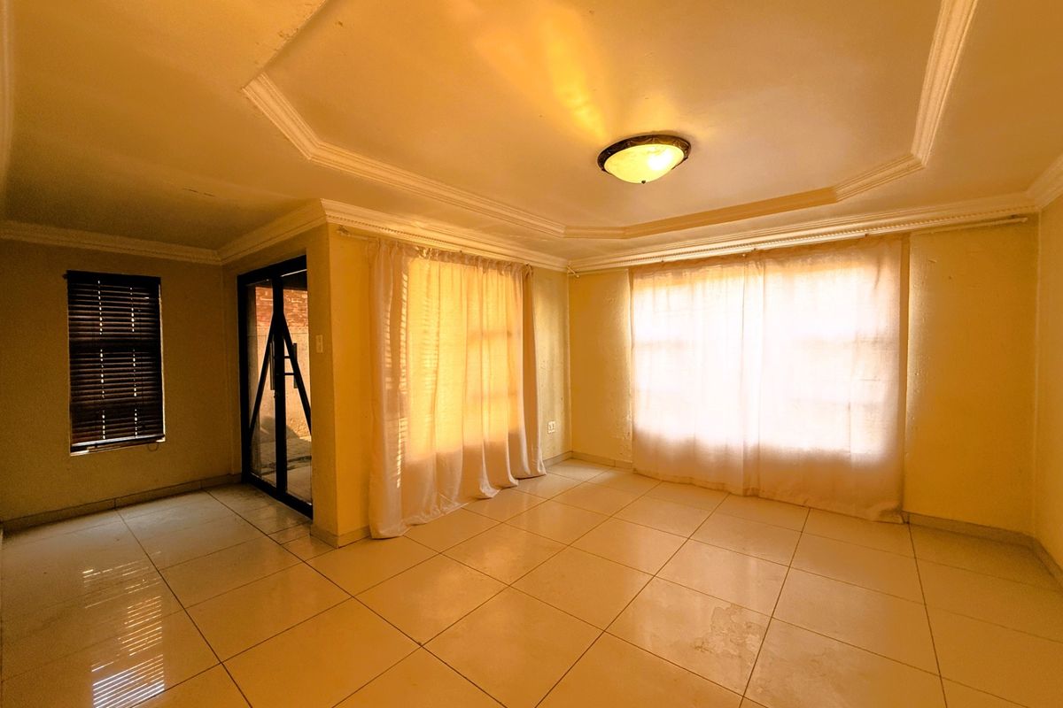 An empty living room featuring tiled flooring, a recessed ceiling with a central light fixture, and large windows with curtains.
