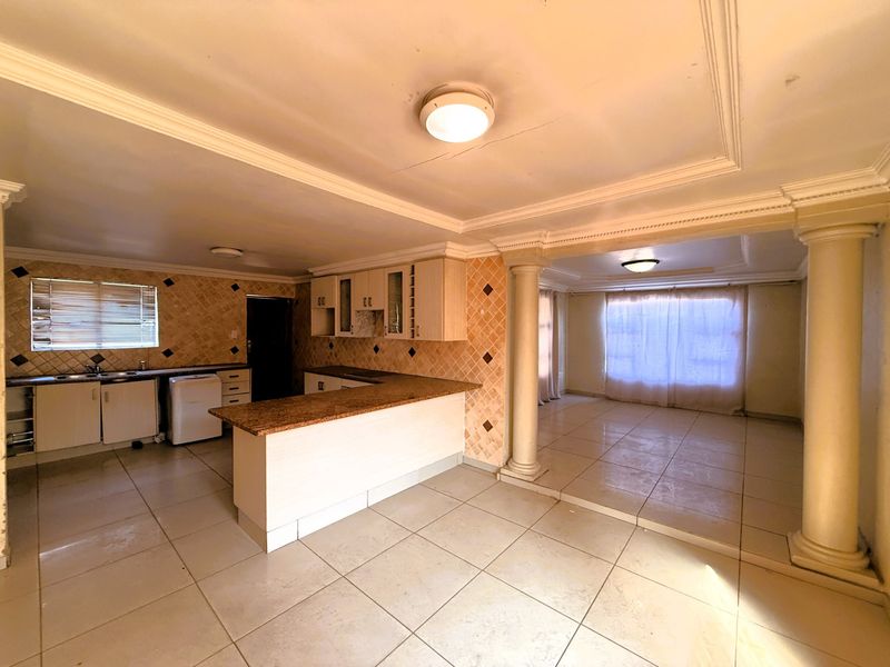 Open plan kitchen and living area featuring granite countertops, built-in cabinetry, decorative columns, and tiled flooring throughout.