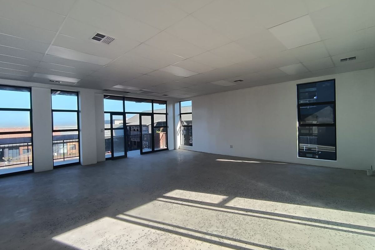 A spacious, empty open-plan commercial office area featuring polished concrete floors, suspended ceiling tiles, and large windows providing ample natural light.