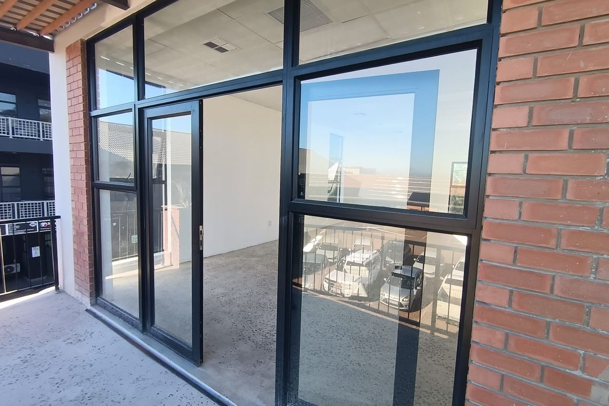 A modern commercial balcony space featuring exposed brickwork, black aluminium framed glass doors, and polished concrete flooring, offering a clean and professional aesthetic.