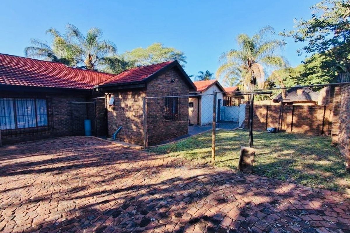 Rear exterior view of the property featuring face-brick construction, a tiled roof, paved driveway area, and a fenced garden space.