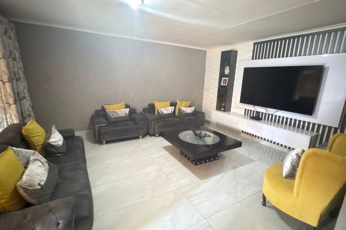 A modern living room featuring large format floor tiles, a custom built-in media wall with integrated shelving, and neutral wall finishes.