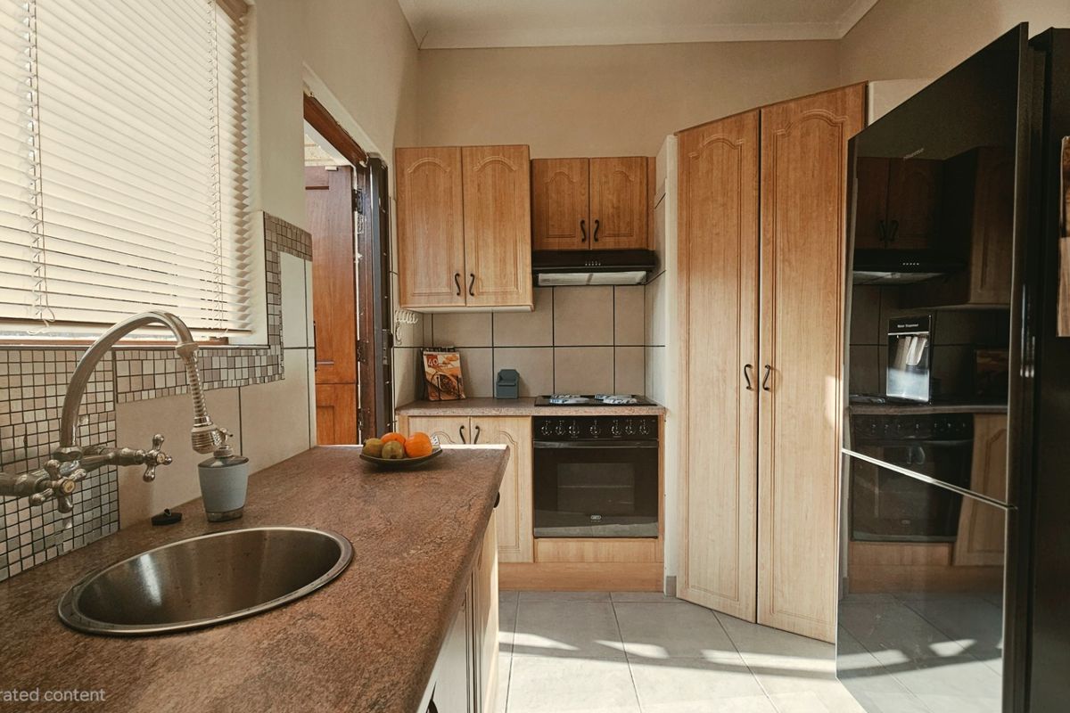 A functional kitchen featuring wooden cabinetry, a built-in oven with hob, extractor fan, and a stainless steel sink with tiled backsplash.