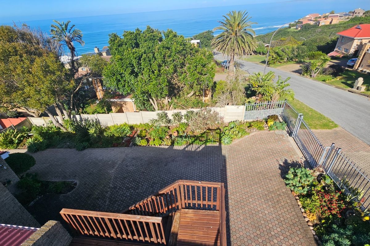 Elevated aerial view of the property driveway, landscaped garden, and surrounding coastal neighborhood with ocean views.