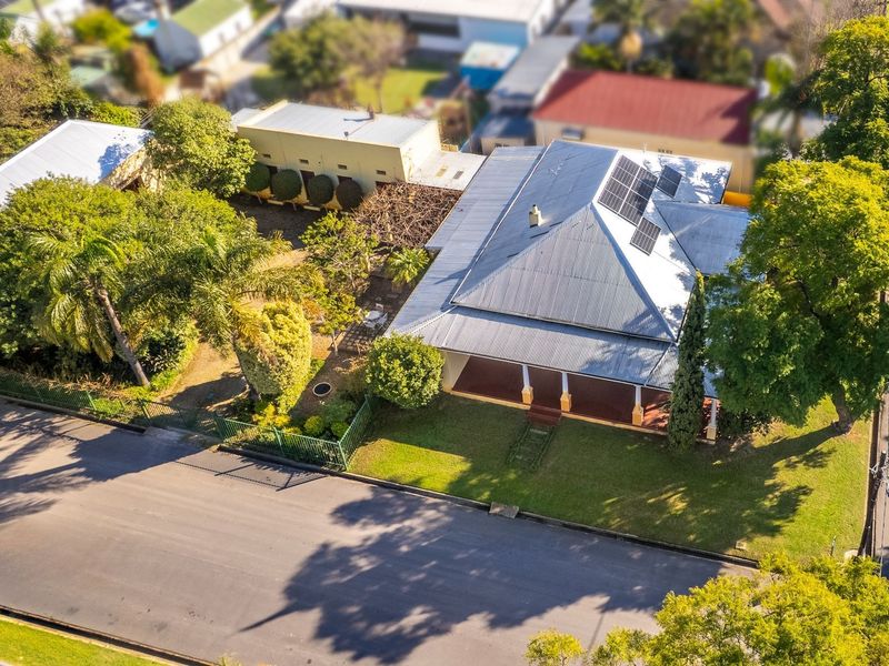 Aerial view of a residential property featuring a corrugated metal roof, solar panels, a covered front veranda, and established garden landscaping.