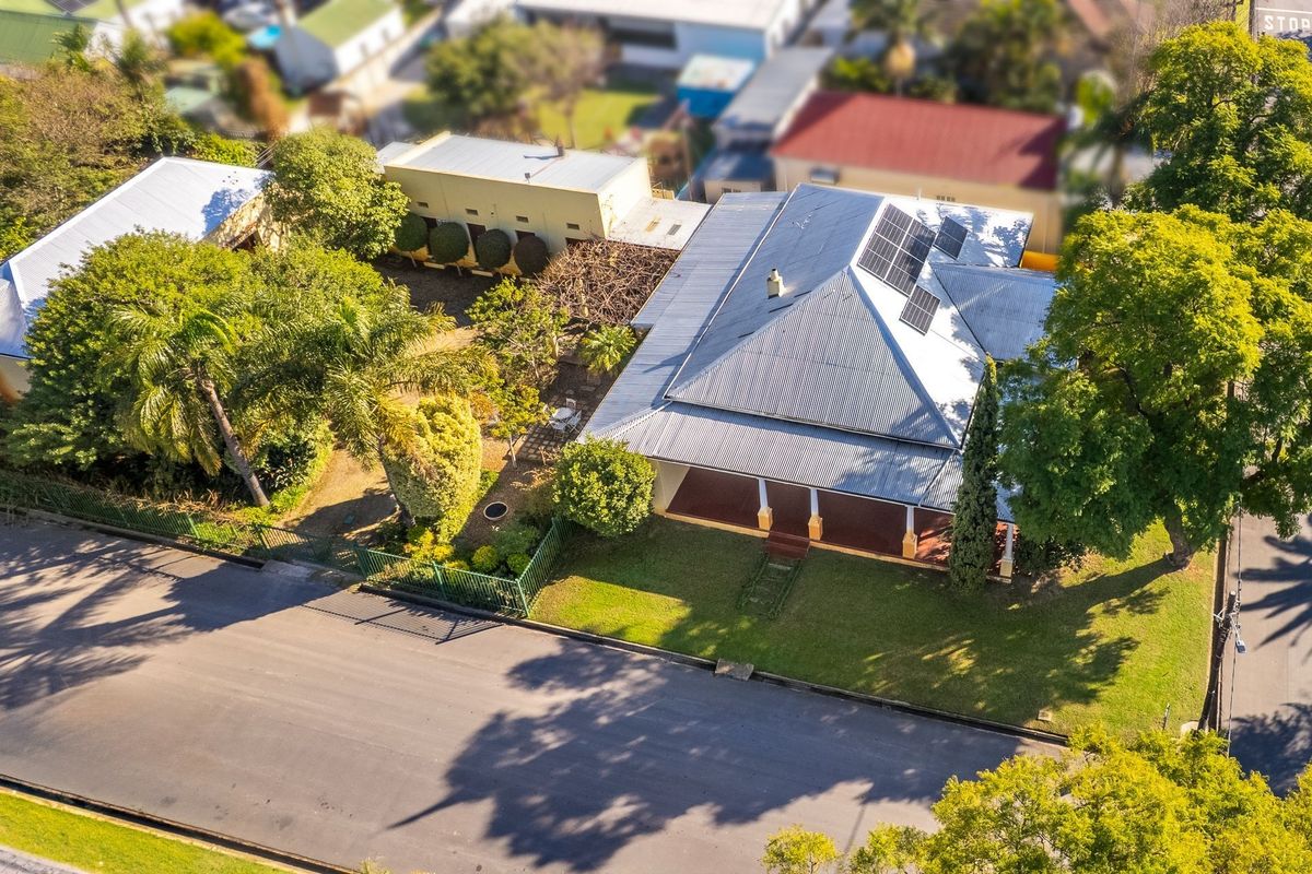 Aerial view of a residential property featuring a corrugated metal roof, solar panels, a covered front veranda, and established garden landscaping.