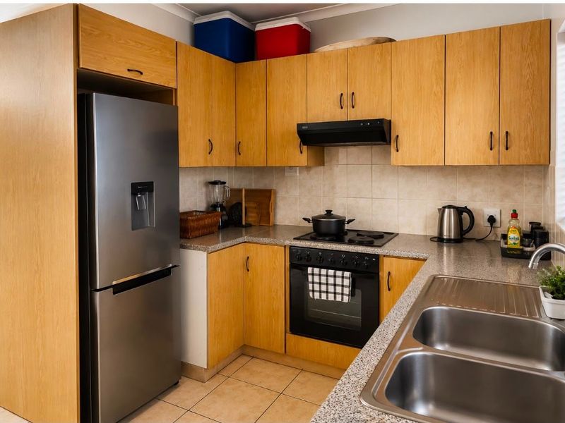 A functional kitchen featuring light wood cabinetry, granite-look countertops, a built-in oven with hob, extractor fan, and a double stainless steel sink.