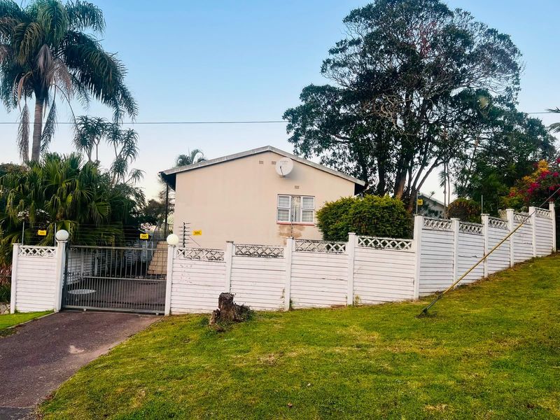 Exterior view of the property featuring a gated entrance, paved driveway, and perimeter boundary fencing set within a landscaped garden area.