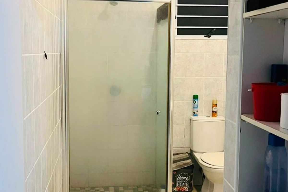 A functional bathroom featuring a glass-enclosed shower, tiled walls and flooring, and a standard toilet, viewed from an adjacent storage area.