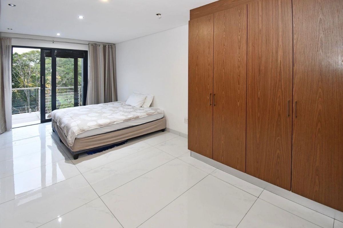 Spacious bedroom featuring large format white floor tiles, built-in wooden cabinetry, and sliding glass doors leading to a private balcony.