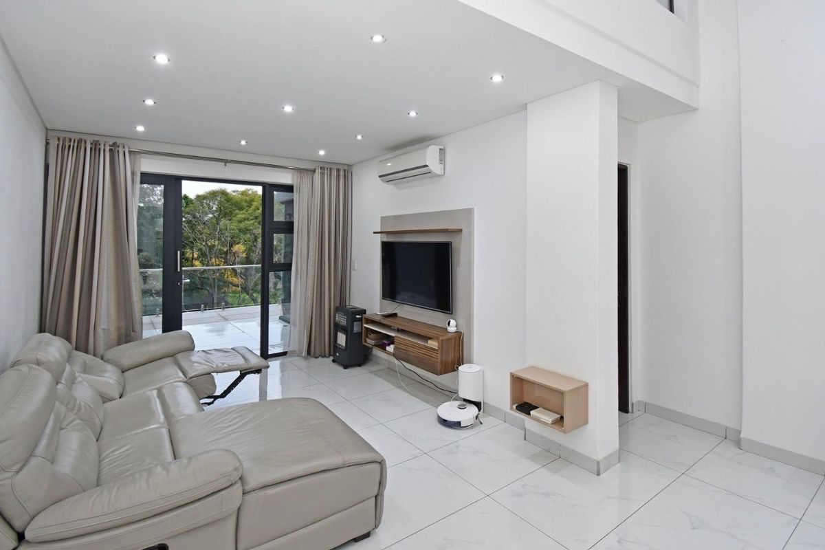 Modern living room featuring tiled flooring, recessed ceiling lighting, a wall-mounted air conditioning unit, and large sliding glass doors leading to a balcony.