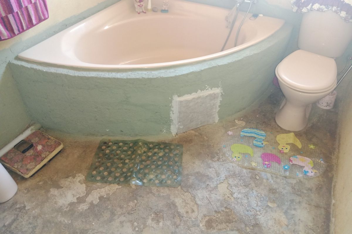 A bathroom featuring a corner bathtub and a standard toilet, currently requiring significant renovation to the flooring and wall finishes.