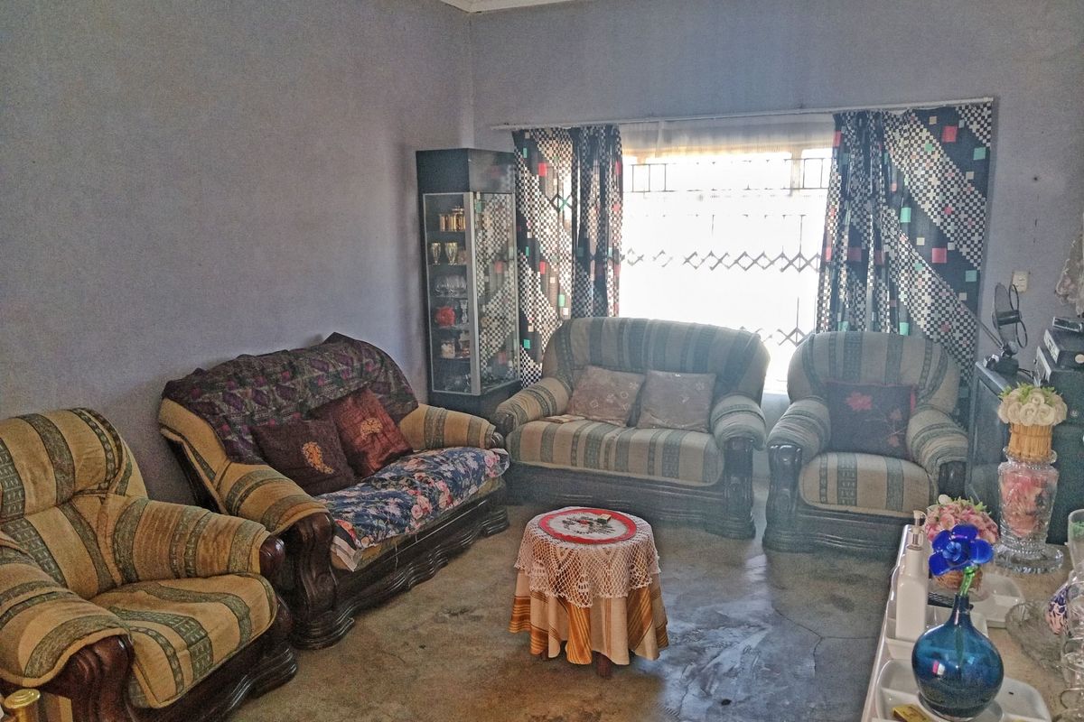 A living room featuring concrete flooring, a large window with security gate, and traditional ceiling cornicing.