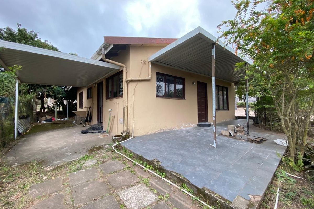 Rear exterior view of the house featuring a covered patio area, metal carport structure, and paved outdoor space with garden surroundings.