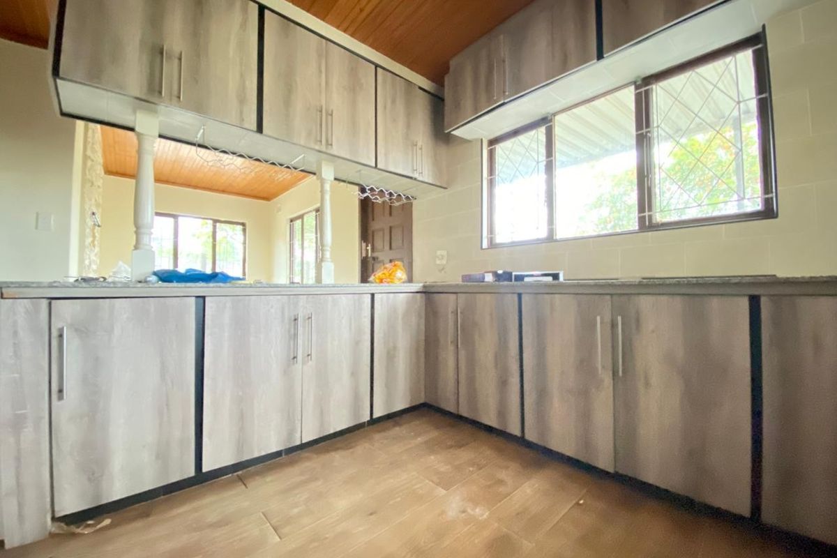 A functional kitchen featuring wood-look cabinetry, stone-style countertops, and a warm timber-paneled ceiling, offering a practical layout with ample storage space.