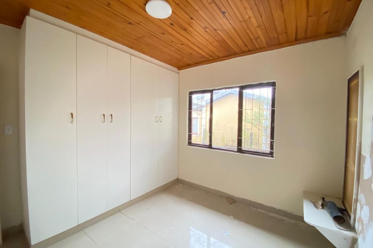 A bright bedroom featuring built-in white cabinetry, tiled flooring, and a timber-paneled ceiling, offering a clean and functional space ready for personalization.