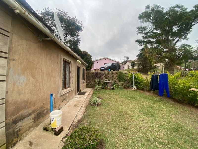 A view of the rear exterior of the house featuring a concrete pathway, a small lawn, and a stone retaining wall.