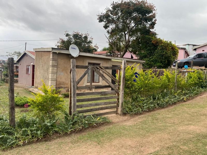 A modest single-story residential property featuring a simple facade, wooden gate entrance, and established garden area.