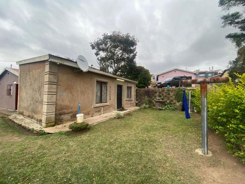 Exterior view of a modest house featuring a small garden, stone retaining wall, and a metal washing line pole.