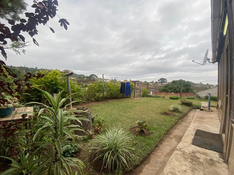 A rear garden area featuring a lawn, established shrubs, and a concrete pathway along the side of the house.