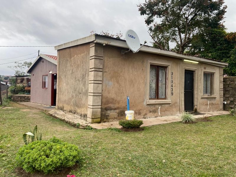 A single-story residential property featuring a weathered exterior facade, security gates, and a surrounding lawn area.