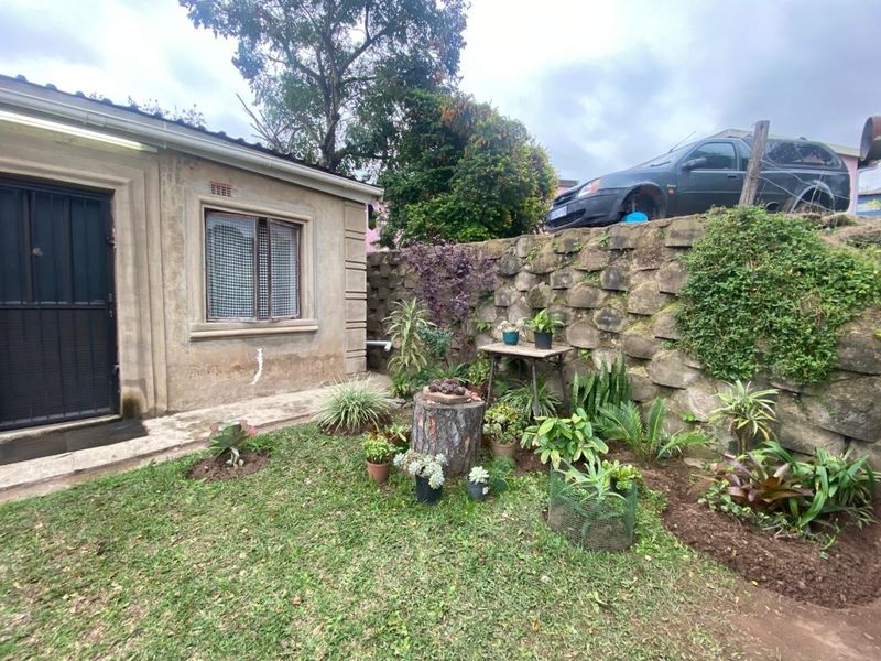 A rear garden area featuring a stone retaining wall, lawn, and exterior access to the dwelling with security gate.