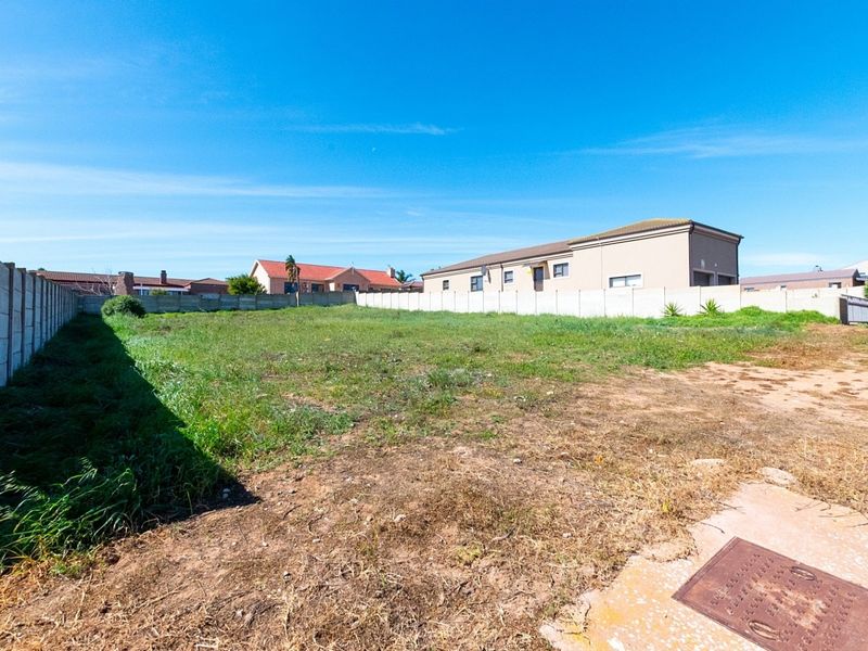 A vacant residential plot enclosed by precast concrete boundary walls, featuring level ground with natural grass and soil coverage.