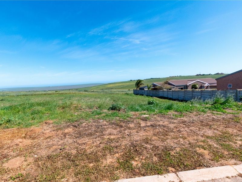 A vacant residential plot featuring open grass land with a precast concrete boundary wall and scenic landscape views.