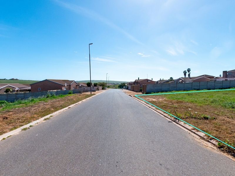 A street view showing the paved road access and boundary of the vacant residential land plot in a developed neighborhood.