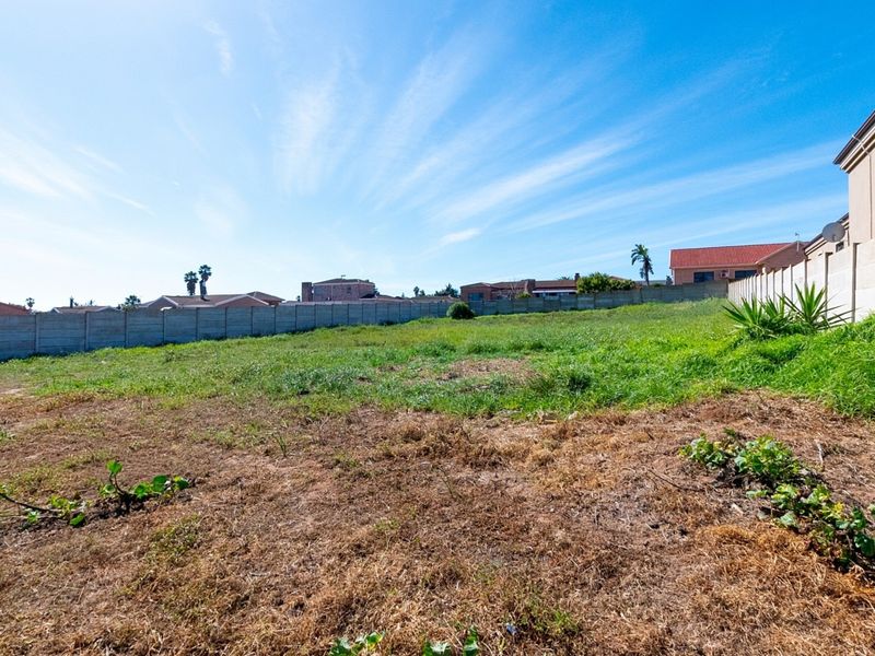 A vacant residential plot featuring a level grassed area enclosed by precast concrete boundary walls in a suburban neighborhood.