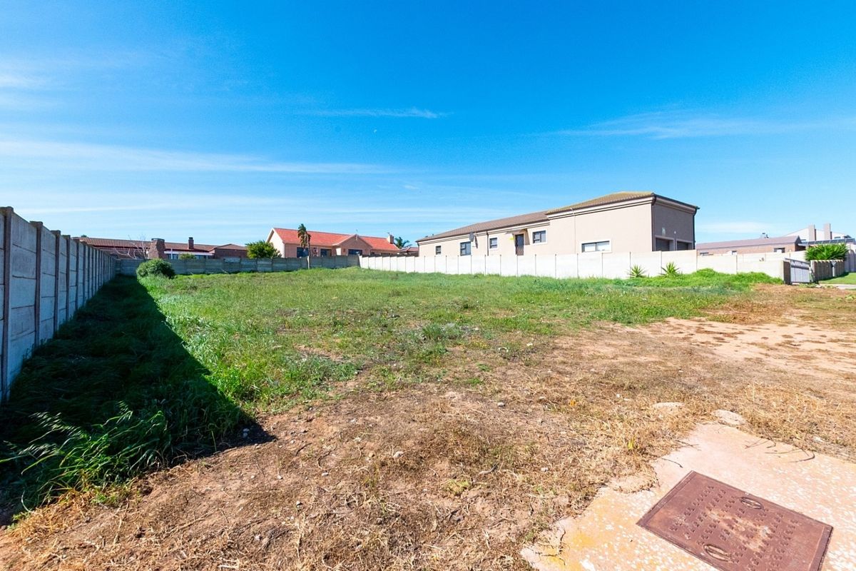 A vacant residential plot enclosed by precast concrete boundary walls, featuring level ground with natural grass and soil coverage.