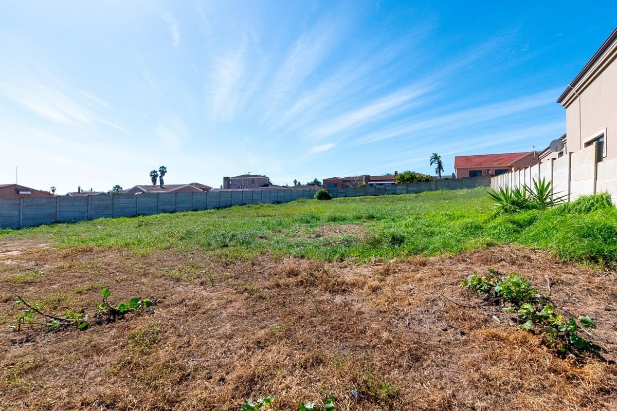 A vacant residential plot featuring a level grassed area enclosed by precast concrete boundary walls in a suburban neighborhood.