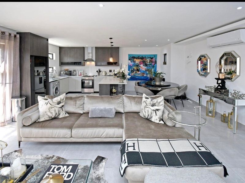 Modern open-plan living area featuring a sleek kitchen with integrated appliances, a central island, and tiled flooring, seamlessly flowing into the dining and lounge space.