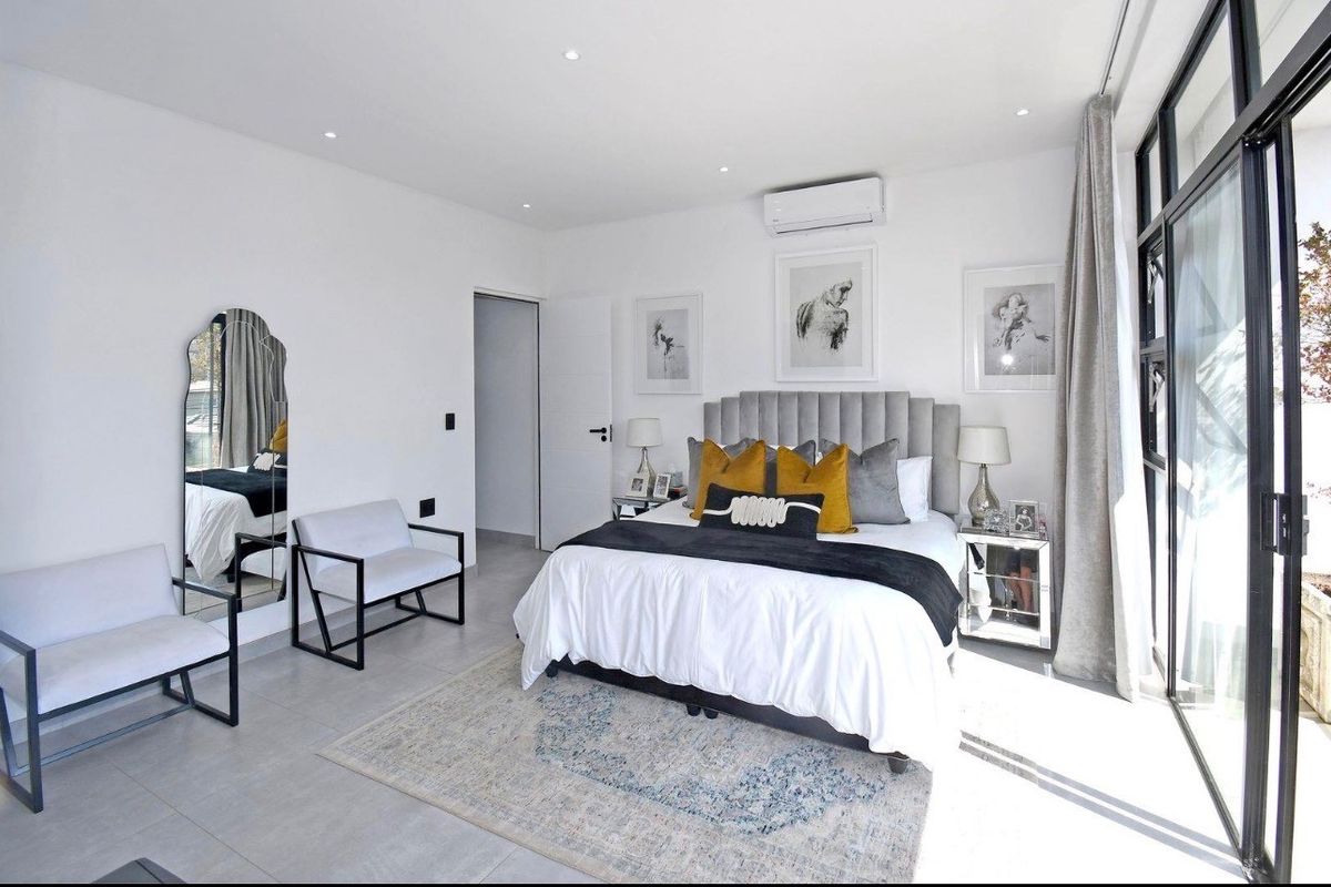 A modern, well-lit bedroom featuring tiled floors, recessed lighting, a wall-mounted air conditioning unit, and large sliding glass doors providing natural light.