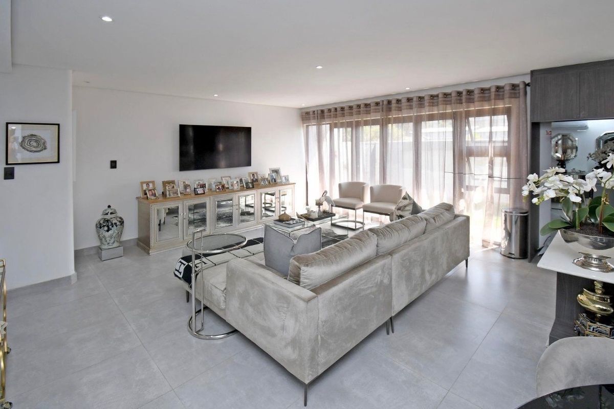 A bright and modern living room featuring large format floor tiles, recessed downlights, and expansive sliding glass doors leading to the exterior.