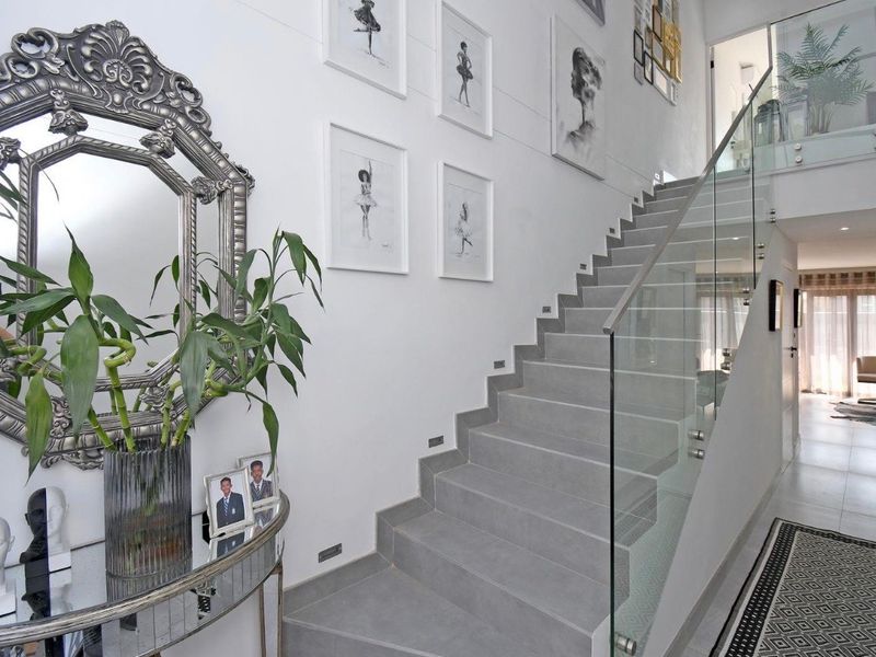 Modern entrance hallway featuring a sleek tiled staircase with a frameless glass balustrade and integrated recessed lighting.